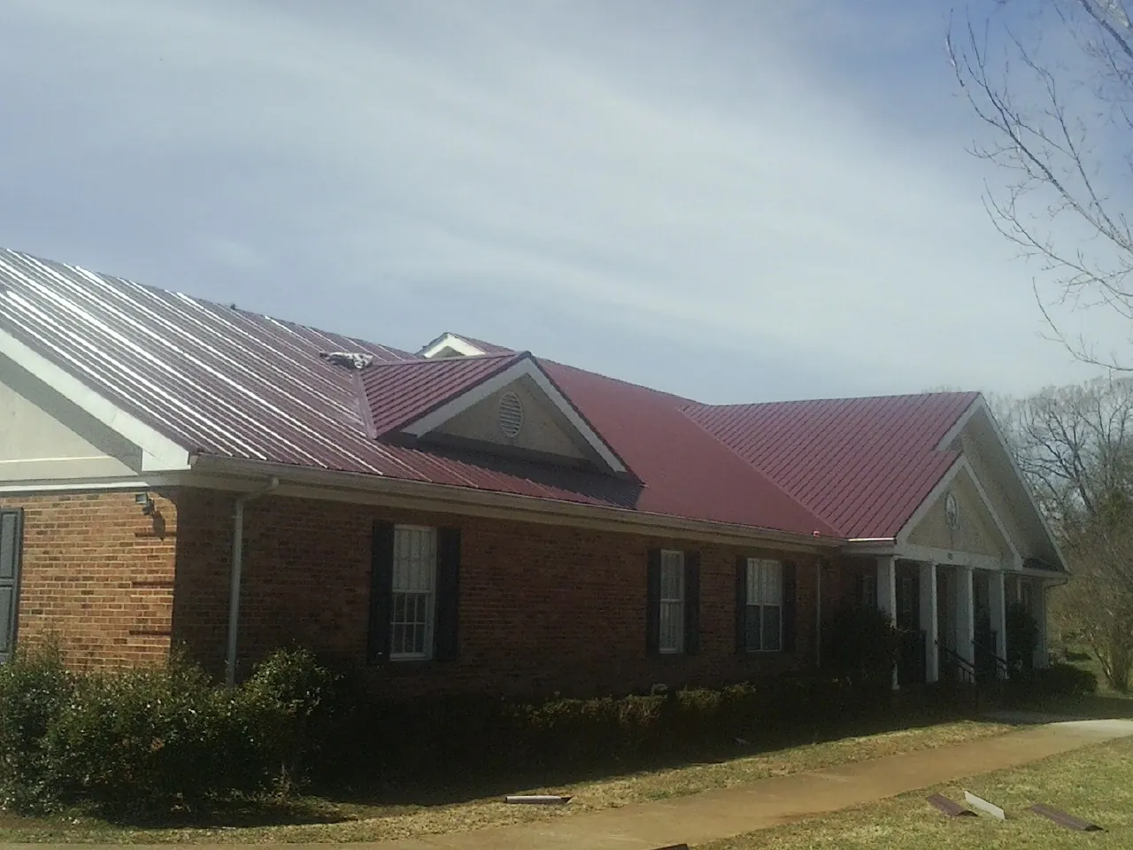 Red metal roof with gabled entries on a long brick building, from a Hail Damage Roof Repair job in Williamsfield