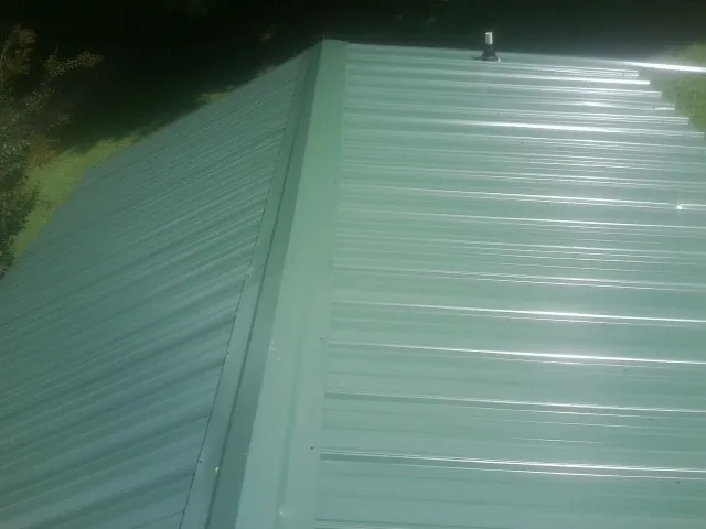 New green metal panels meeting at the ridge of a roof — Flat Roof Repair work by our crew in Williamsfield