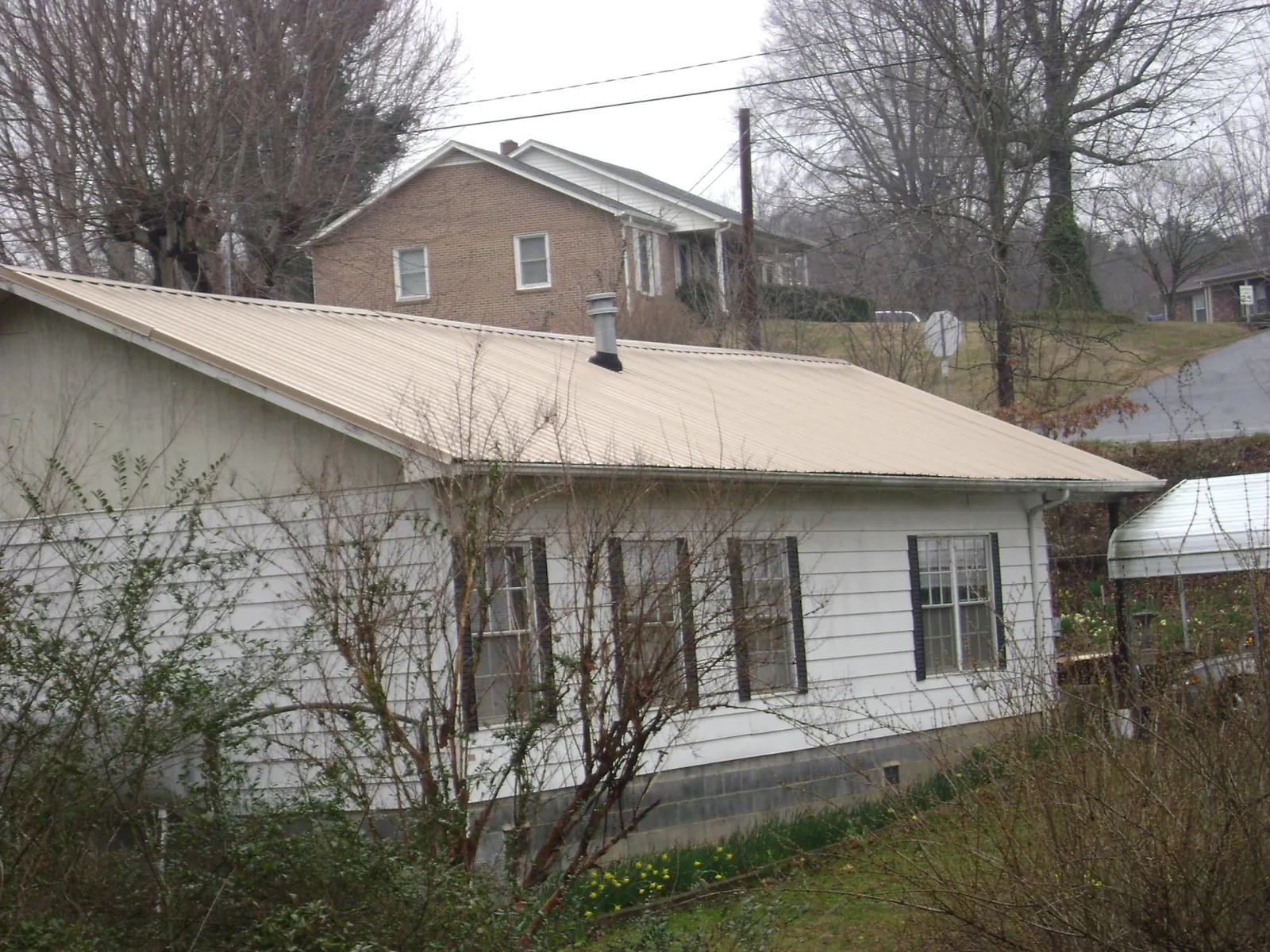 Tan metal roof on a white sided house set into a hillside — Commercial Roofing by Roofing Brothers in Williamsfield