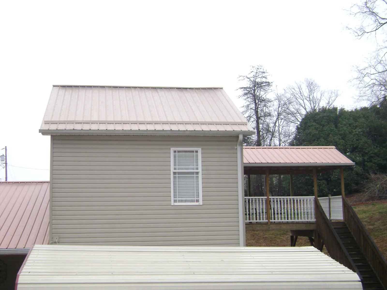Tan metal roofs on a two story addition and attached porch, from a Roof Replacement job in Williamsfield